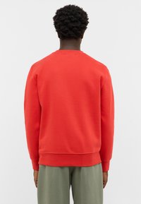 Czerwony bawełniany polar z długimi rękawami, ściągaczami na rękawach i dolnej części. Klasyczny okrągły dekolt, minimalistyczny styl i gładka faktura.