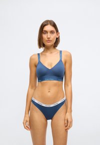 Bralette en coton bleu avec des bretelles ajustables et un détail de logo. Bikini assorti avec une taille blanche et un logo. Texture lisse, design décontracté.