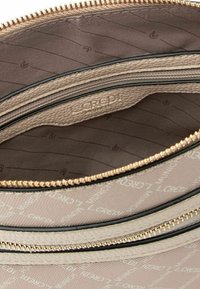 Interno di una borsa beige testurizzata con zip dorate, dotata di due scomparti e una fodera marrone scuro con un motivo decorativo.