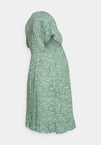 Vestido floral verde com um corte solto, mangas curtas e um acabamento em babados. O tecido tem uma superfície texturizada com padrões brancos e verdes mais escuros.