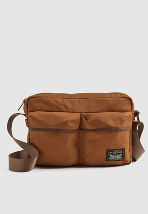 Brun Levi's axelväska med justerbar rem, två framfickor och en Levi Strauss & Co.-logopatch i det nedre högra hörnet.