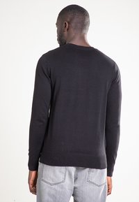 Czarny dzianinowy sweter z długimi rękawami, okrągłym dekoltem i prążkowanym dołem. Noszony z jasnoszarymi dżinsami, pokazany od tyłu.