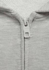 Veste zippée grise en tissu tricoté texturé, avec une fermeture éclair lisse et une impression "MNG" sur la tirette.