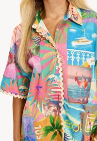 Chemise à manches courtes colorée avec plusieurs motifs vifs, col festonné et imagerie tropicale, confectionnée en tissu léger.