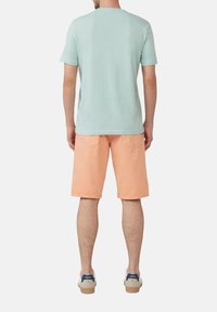 Lichtblauwe katoenen t-shirt gecombineerd met perzikkleurige shorts. De shorts hebben zakken en een soepele textuur, compleet met beige sneakers.