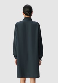 Abito verde scuro a maniche lunghe con colletto strutturato e vestibilità ampia. Tessuto morbido che arriva a metà coscia; maniche con polsini per un'elegante finitura.