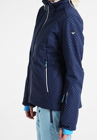 Marineblaue Jacke mit einem Hahnentrittmuster, ausgestattet mit einem hohen Kragen, Reißverschlusstaschen und kontrastierenden hellblauen Akzenten.