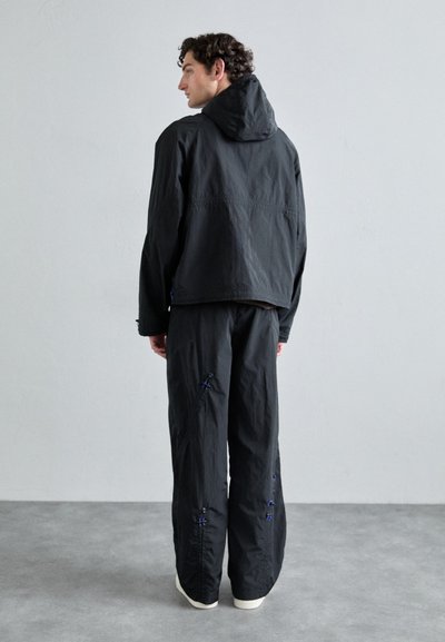 Men's black jacket and pants set, featuring a hood and blue stitching accents. Made from lightweight fabric, with a relaxed fit.