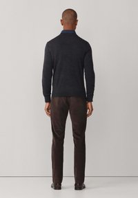 Tmavě šedý pletený svetr s límcem, dlouhými rukávy a žebrovanými manžetami, v kombinaci s tmavě hnědými kalhotami. Hladká textura a přiléhavý design.