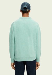 Maglione lavorato a maglia di colore azzurro con colletto, polsini e orlo a costine. Indossato con un cappellino blu con del testo sul retro.