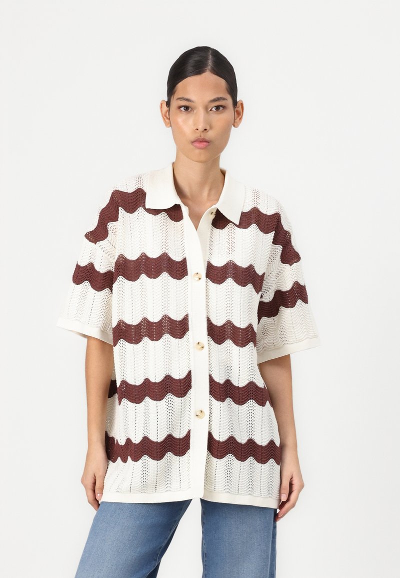 Maglietta a maniche corte lavorata a maglia in crema con strisce ondulate bordeaux, con chiusura con bottoni e colletto strutturato. Texture morbida e traspirante.