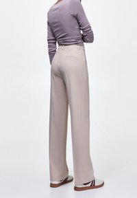 Chemise longue à manches longues de couleur violet clair assortie à un pantalon beige taille haute à jambes larges. Le modèle porte des baskets blanches avec des accents bordeaux.