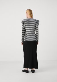 Top de manga larga a rayas blancas y negras con acentos de hombros fruncidos, combinado con una falda negra fluida y zapatos negros, visto desde la parte posterior.