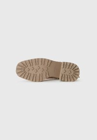 Semelle de botte marron avec un motif de crampons profond et des grips en forme de croix, taille 37 marquée au fond, isolée sur un fond blanc.