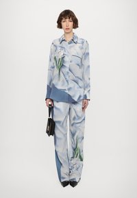 Blue floral print shirt and matching trousers, both in satin-like material. Features a pocket and is paired with a small black handbag.