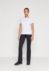 Balta kokvilnas T-kreklu ar "DKNY" logotipu no struktūrfasām, apvienots ar pieguļošu melnu ribotu biksēm un melniem sporta apaviem.