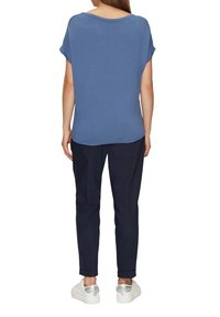 Niebieska bluzka krótki rękaw o luźnym kroju i okrągłym dekolcie, zestawiona z ciemnymi spodniami i białymi trampkami z metalicznymi akcentami.