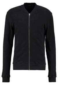 Black bomber jacket made of textured fabric, featuring a central zip closure, ribbed cuffs, and a round neckline. Minimalist design.