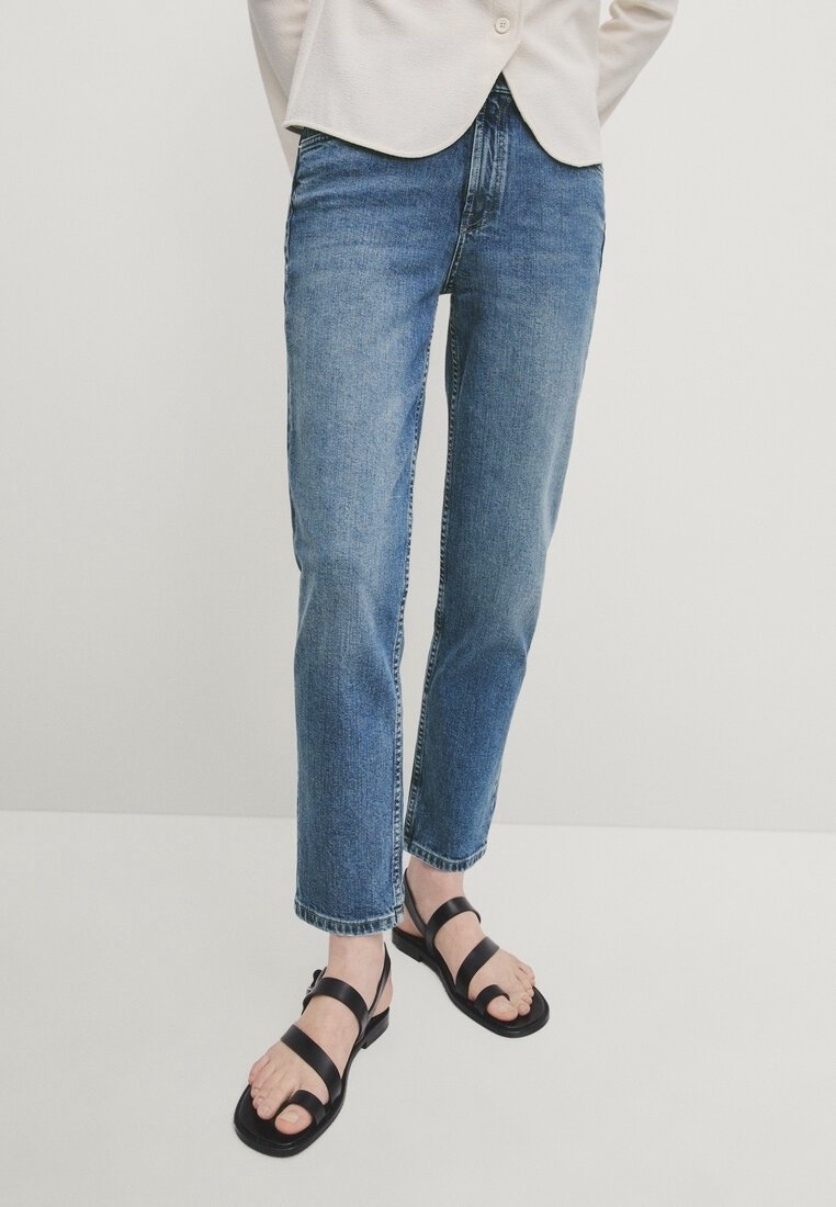 Light blue jeans with a straight cut and faded texture, paired with black strappy sandals. The outfit features a beige top.