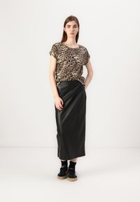 Leopardų rašo marškiniai su trumpomis rankovėmis derinami su juoda odine maksi sijonu. Modelis vilki juodas sportines batus su platformos padu ir kulkšnies kojinėmis.