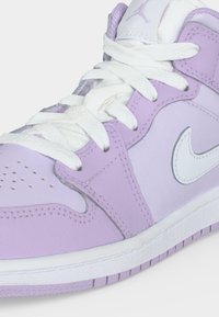 Κοντινή λήψη ενός άνω αθλητικού παπουτσιού σε λιλά και λευκό χρώμα με λευκά κορδόνια και λογότυπο Nike σε λευκό στην πλευρά.