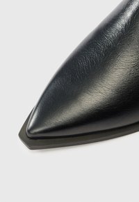 Pantof negru din piele cu vârf ascuțit, textură netedă și design elegant, având o talpă din cauciuc negru contrastantă și un accent unghial la călcâi.