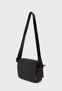 Borsa a tracolla nera con chiusura a zip, tessuto strutturato con motivo a logo ripetuto e tracolla regolabile con dettagli rossi.