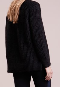 Schwarzer Strickpullover mit strukturiertem Muster, gerippten Details und lockerer Passform. Hergestellt aus weichem, dickem Garn und mit langen Ärmeln.