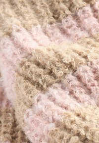 Texturerad stickad tyg i beige och ljusrosa, med upphöjda slingor och sammanflätade trådar som skapar ett mjukt, fluffigt utseende.