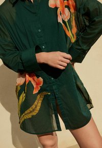 Groene button-up blouse van doorzichtig stof, met bloempatronen in oranje en geel. Losse pasvorm met een hoge-lage zoom en opgerolde mouwen.