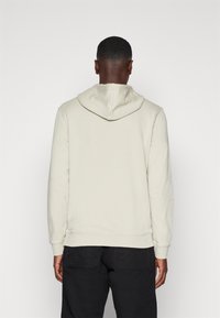 Ljusbeige hoodie med dragsko i huven, ribbnade ärmar och nederkant. Slät textur med en avslappnad passform, buren över svarta byxor.