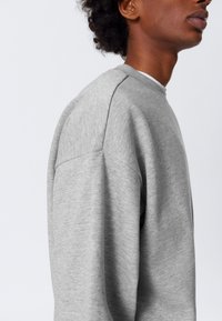 Grijze sweatshirt met een zachte textuur, voorzien van een ronde hals en verlaagde schoudernaden, zijaanzicht tegen een effen achtergrond.