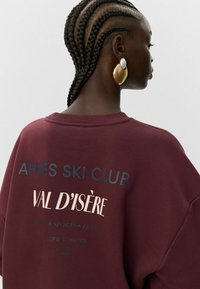 Sudadera color marrón con las impresiones "APRES SKI CLUB" y "VAL D'ISÈRE" en colores contrastantes; cuello de canalé; corte relajado; tela suave.