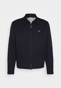 Mørkeblå zip-up jakke med krage, sidelommer og et lite logo på brystet. Glatt tekstur, rett passform og lange ermer.