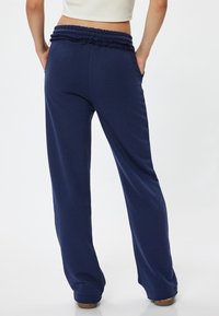Marineblauwe joggingbroek met een gerimpelde elastische tailleband, twee zijzakken en een losse, rechte pasvorm. Zacht materiaal met een gladde textuur.