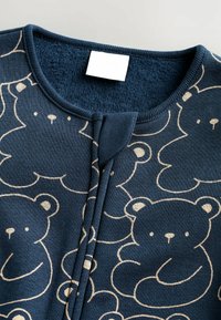 Marineblaue Baumwollbekleidung mit einem sich wiederholenden hellbeigen Bärenmuster, rundem Halsausschnitt, strukturiertem Finish und vorderem Druckknopfverschluss.