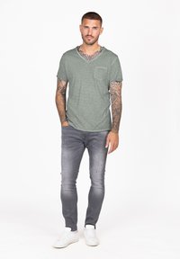 Jasnozielona koszulka z dekoltem w serek z kieszonką na piersi, zestawiona z szarymi slim fit jeansami o zniszczonym wyglądzie i białymi trampkami.