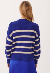 Blauw en crèmekleurig gestreepte trui met een geribbelde textuur, oversized pasvorm en een ronde halslijn. Beschikt over verlaagde schouders en lange mouwen.