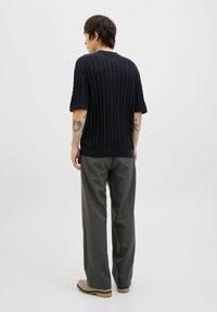 Pulover scurt cu mânecă scurtă, texturat, de culoare neagră, având un design de cabluri cu dungi, asociat cu pantaloni gri și pantofi bej, văzut din spate.