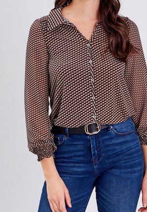 Femme portant un chemisier à manches longues à motifs avec des boutons, rentré dans un jean bleu, accessoirisée d'une ceinture noire avec une boucle dorée.