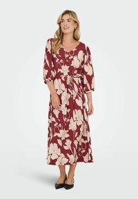 Lång burgundröd klänning med vita blommönster, v-ringad, 3/4 ärmar, åtsittande midja, slät textur och hamn som når anklarna. Kombinerad med svarta klackar.
