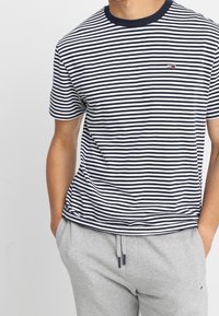 Pruhované tričko s krátkým rukávem v námořnické modré a bílé barvě vyrobené z bavlny, s malým logem na levé hrudi.