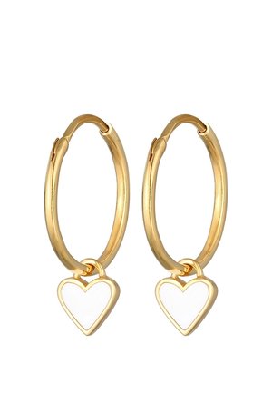 Boucles d'oreilles anneaux dorés avec de petits charms blancs en forme de cœur suspendus à chaque anneau sur un fond blanc.
