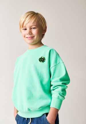 Mintgrøn sweatshirt lavet af blødt stof, med rund hals og ribbede manchetter. Bemærkelsesværdige detaljer inkluderer et farverigt patch med ordet "SWEET."