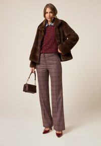 Abrigo de piel sintética marrón, suéter con estampado burdeos, pantalones de cuadros marrones y tacones burdeos. Incluye un bolso pequeño con acentos dorados.