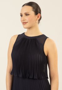 Marineblauem plissiertes Kleid mit ärmellosem Design, das durchscheinende Akzente an den Schultern und eine glatte Textur aufweist. Elegante und strukturierte Silhouette.