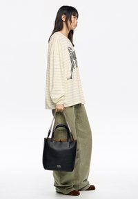 Czarna skórzana torba typu tote z srebrnymi uchwytami w formie łańcucha, z fakturowaną powierzchnią i kontrastowym brązowym wnętrzem, trzymana przez osobę w codziennym stroju.