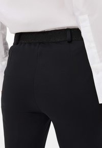 Schwarze Hose mit einem strukturierten Bund und schlankem Design. Sie zeichnet sich durch einen glatten, matten Stoff und präzise Nähte aus.