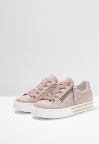 Jasnoróżowe zamszowe sneakersy z okrągłym noskiem, tonalnym wzorem sznurowania, z boku zapięcie na zamek oraz białą fakturowaną podeszwą z beżowymi paskami.