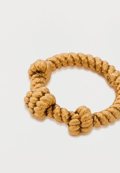 Βραχιόλι με επίστρωση χρυσού σε σχεδίαση περίτεχνου σχοινιού με τρεις μεγάλους κόμπους πάνω σε απλό λευκό φόντο.